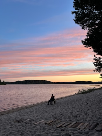 A peaceful lakeside at sunset with a single wooden bench inviting quiet reflection.