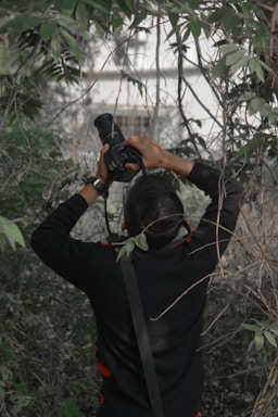 A close-up shot of a photographer in the wild, camera poised, surrounded by lush greenery and wildlife.