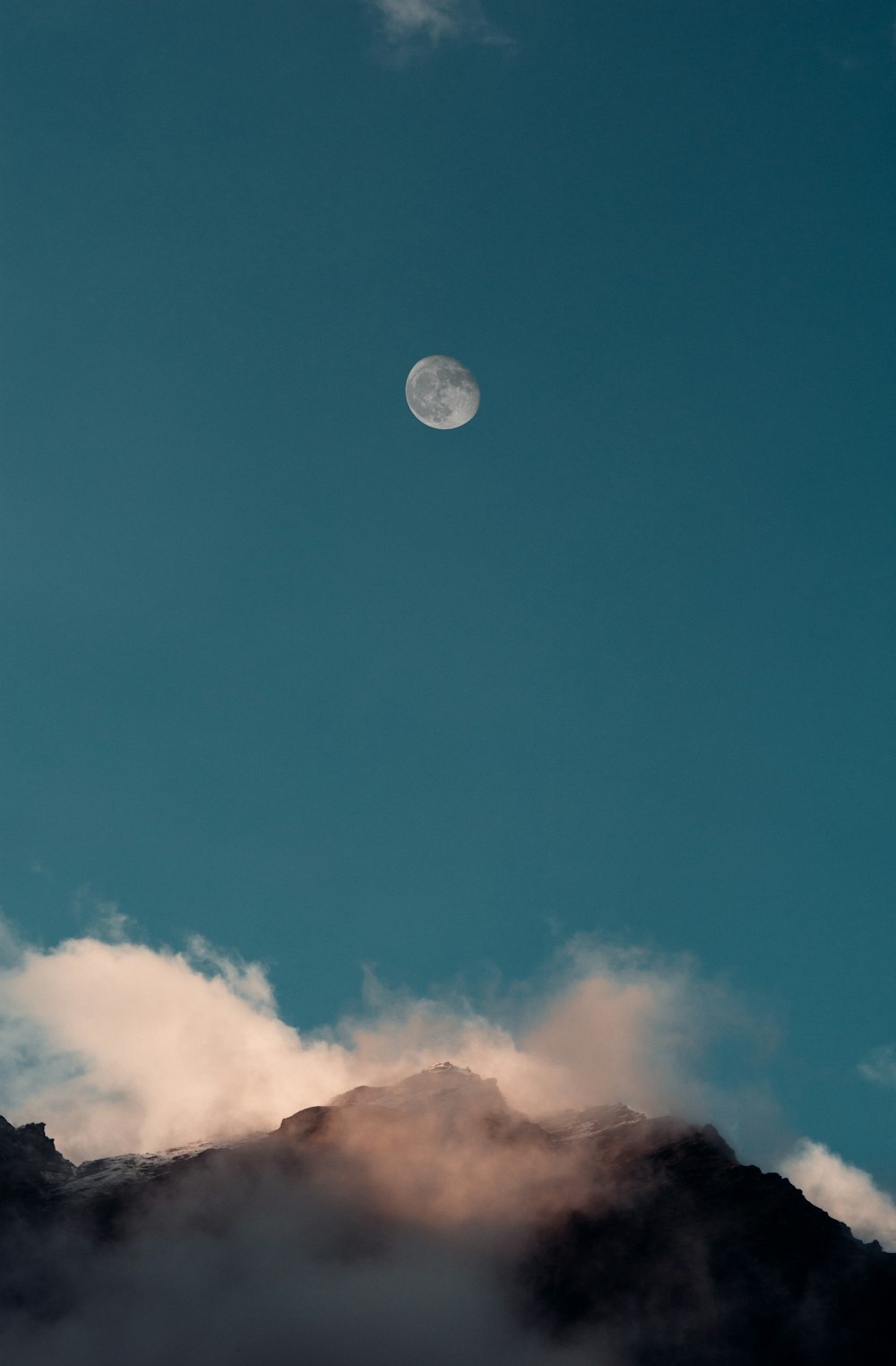 a full moon is seen above a mountain