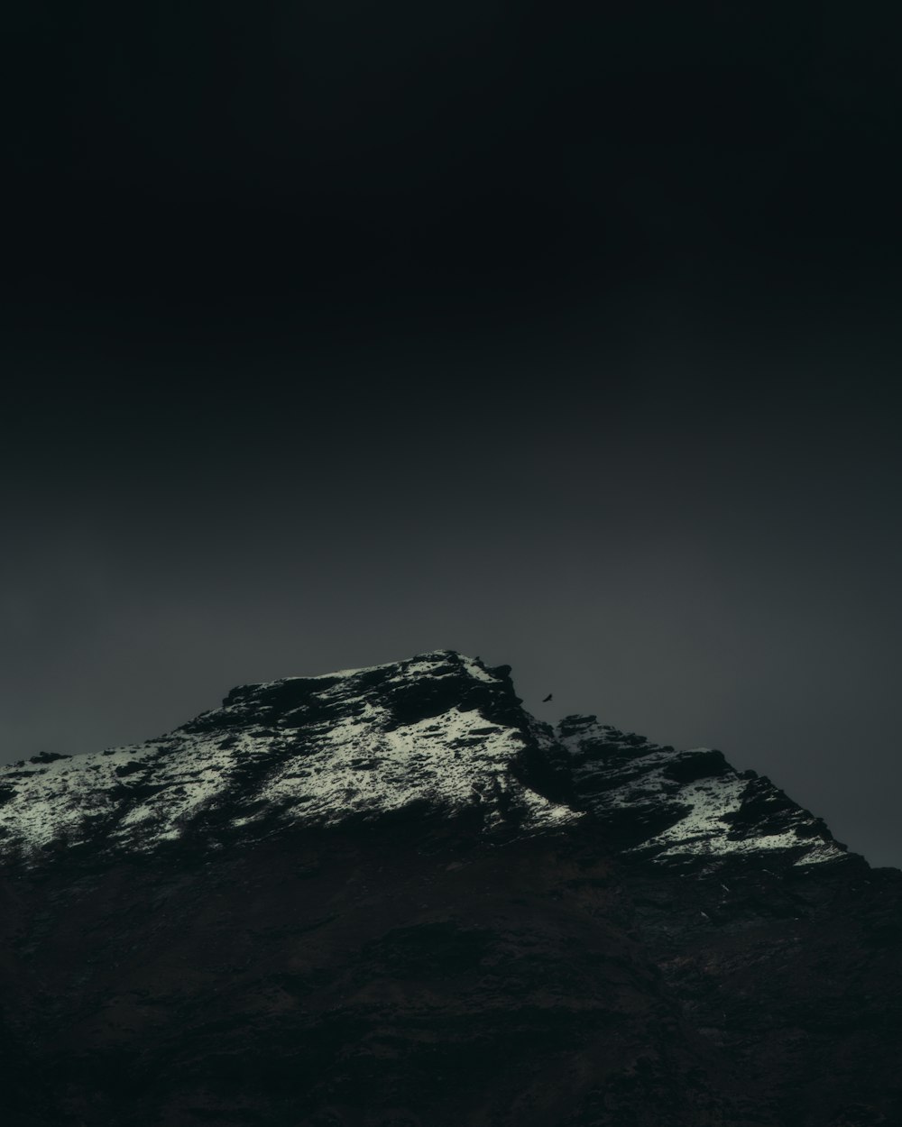 a very tall mountain covered in snow under a dark sky