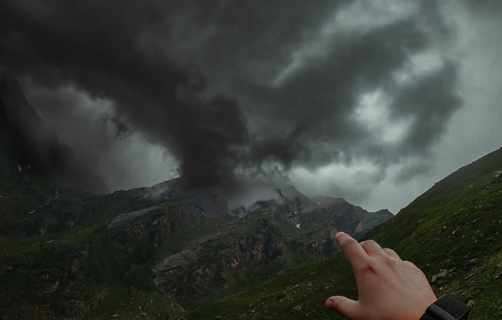 a hand pointing at a black cloud in the sky