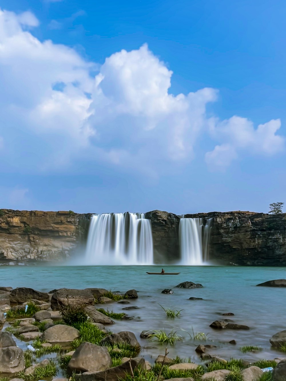 a large waterfall with a man in a boat in the water