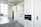 A modern kitchen features sleek white cabinetry, a built-in oven, and a large countertop island with a stovetop. The space is brightly lit by a large window, and a vase with green foliage sits on the counter. Stainless steel appliances add to the contemporary feel.