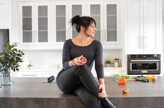 a woman sitting on a kitchen counter holding a piece of fruit
