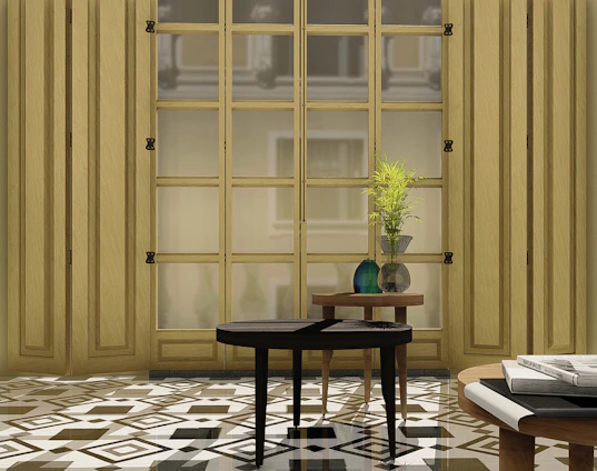 A stylish interior setting features a large wooden window with multiple panes, allowing soft natural light to filter in. The foreground is adorned with two wooden tables; one holds a decorative plant arrangement in a glass vase, while the other supports a stack of books and magazines. The floor is patterned with geometric tiles, adding to the room's elegant ambiance.