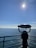 A telescope mounted on a pier overlooks a vast expanse of ocean under a clear blue sky. The sun is shining brightly, reflecting off the water's surface, creating a serene and peaceful atmosphere.