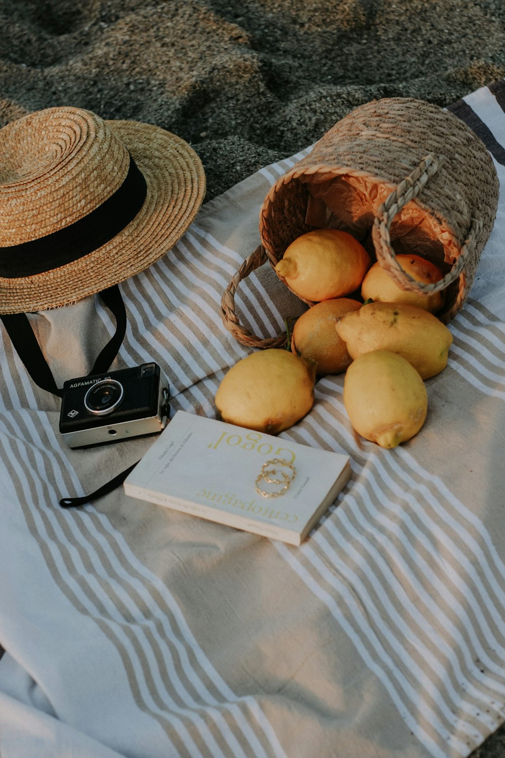 a bag of lemons, a book, and a straw hat on a towel