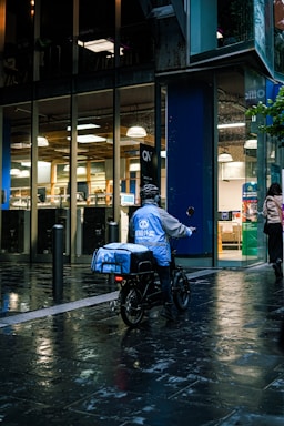 A friendly delivery rider handing over groceries at night outside a Manchester apartment.
