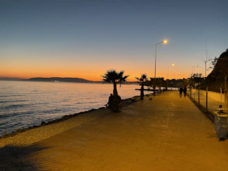 A peaceful seafront promenade at sunset in İzmir with calm waters and walking people.
