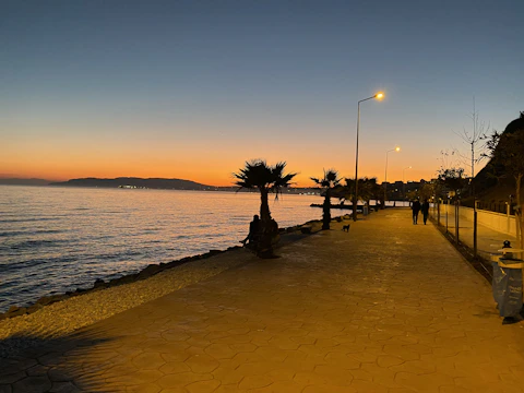 A peaceful seafront promenade at sunset in İzmir with calm waters and walking people.