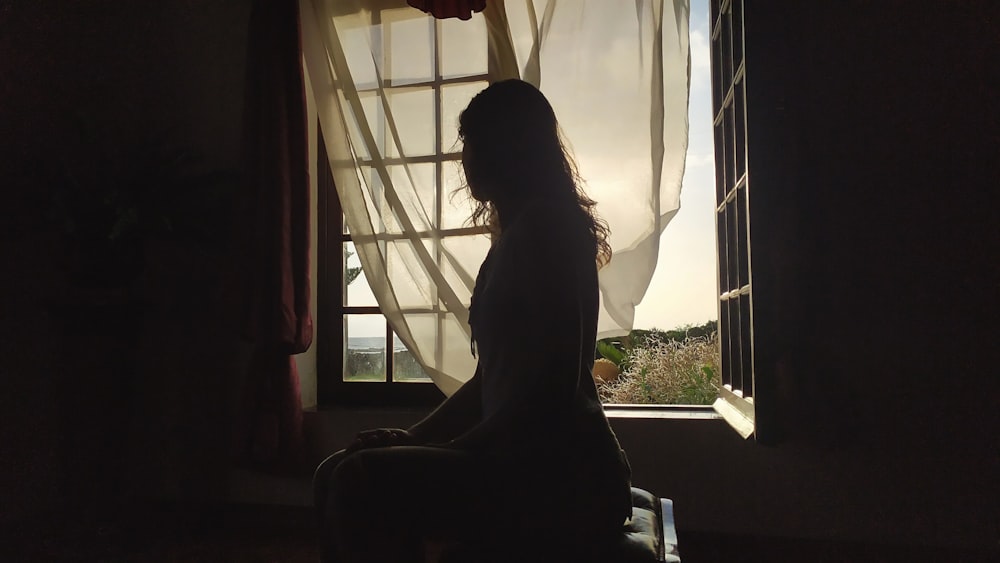 a woman sitting in front of a window in a dark room