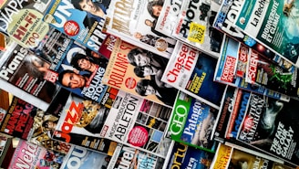 A variety of magazines are displayed in a chaotic but organized manner, featuring popular titles with colorful covers. The magazines are stacked and overlapping, showcasing diverse topics like music, science, travel, and lifestyle.