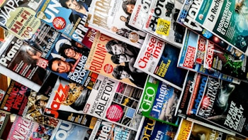 A variety of magazines are displayed in a chaotic but organized manner, featuring popular titles with colorful covers. The magazines are stacked and overlapping, showcasing diverse topics like music, science, travel, and lifestyle.