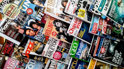 A variety of magazines are displayed in a chaotic but organized manner, featuring popular titles with colorful covers. The magazines are stacked and overlapping, showcasing diverse topics like music, science, travel, and lifestyle.