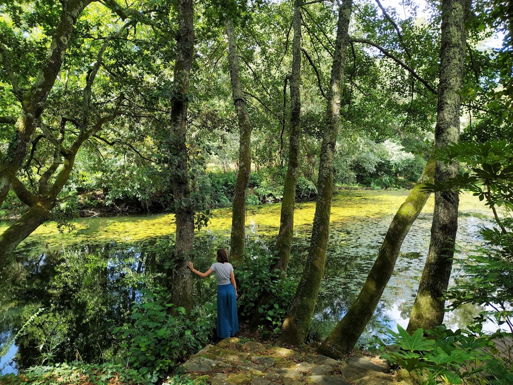 a woman standing next to a river surrounded by trees