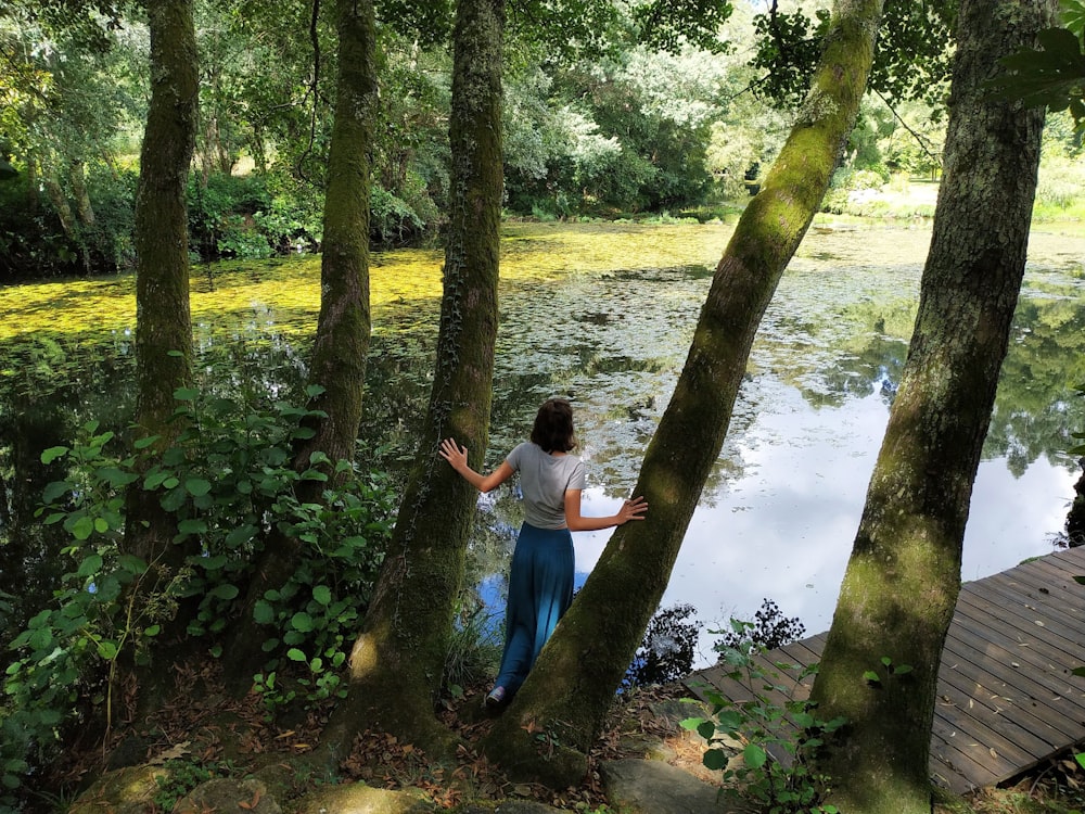 a woman standing next to a tree next to a body of water