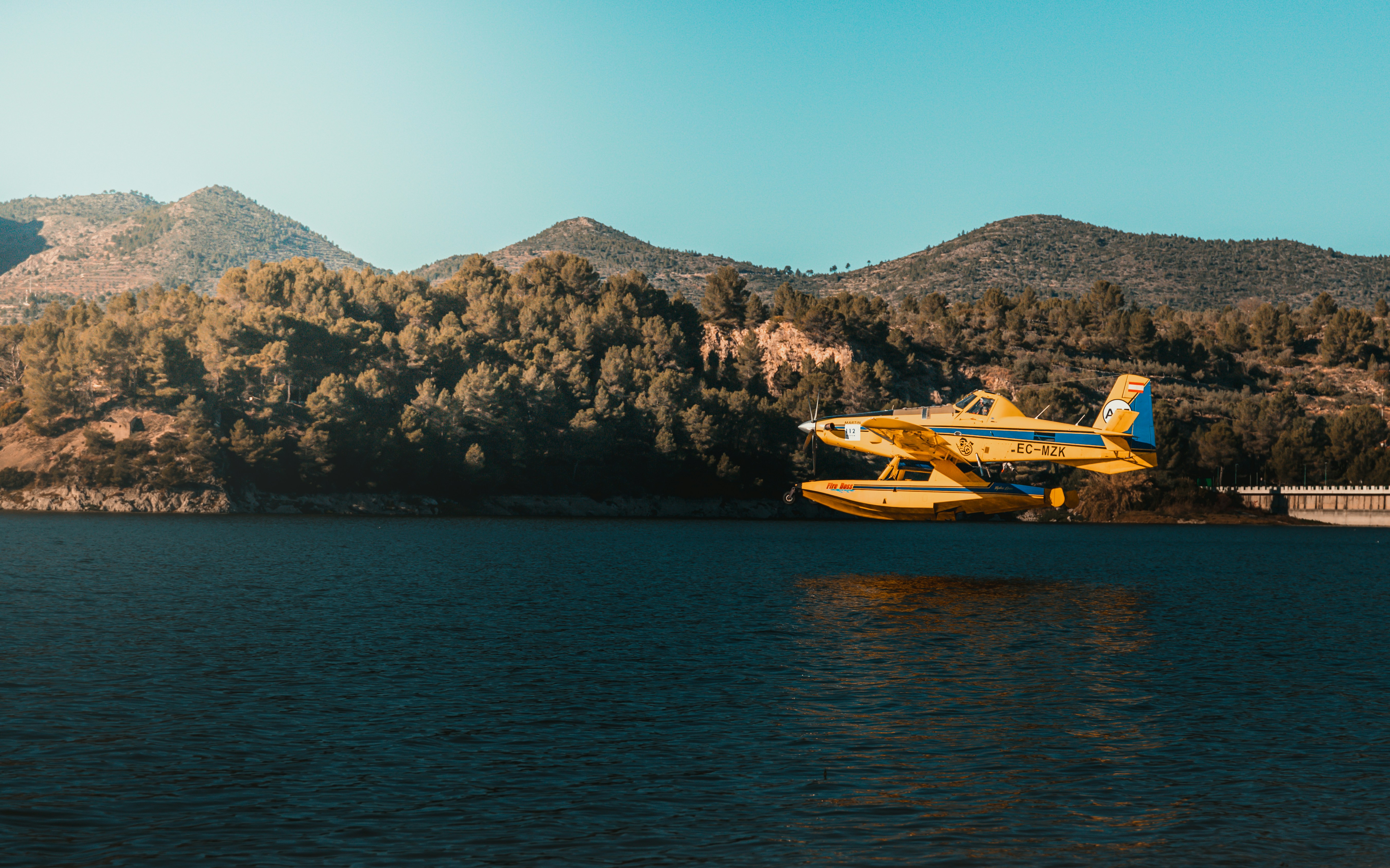 a yellow and blue plane flying over a body of water