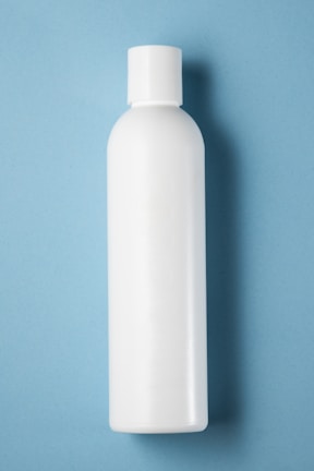 A plain white plastic bottle with a cylindrical shape and a cap on top, positioned vertically against a light blue background.
