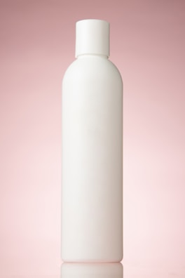 A plain, white cylindrical bottle with a pink background. The bottle has a rounded cap and no labels or markings, reflecting a minimalist design.