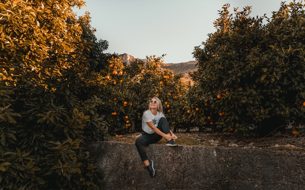 a woman sitting on a wall surrounded by orange trees