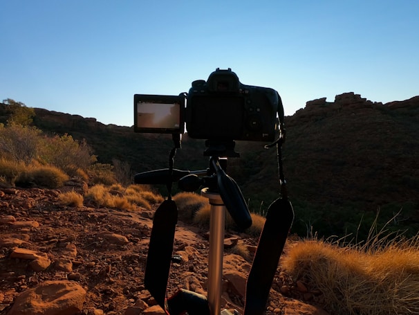 A photographer adjusting a tripod on a sandy desert dune under a clear blue sky.