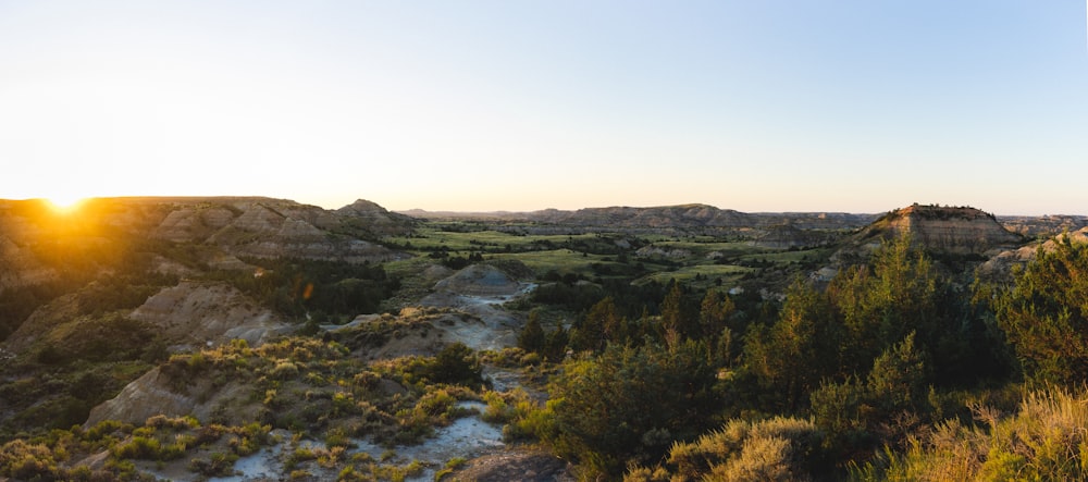 the sun is setting over the hills and trees