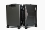 Two sleek, black hard-shell suitcases positioned side by side on four wheels each, showcasing modern design and durability with a smooth matte finish.