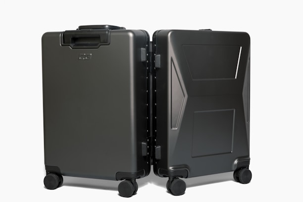 Two sleek, black hard-shell suitcases positioned side by side on four wheels each, showcasing modern design and durability with a smooth matte finish.
