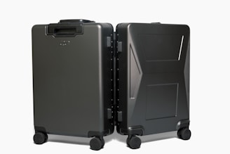 Two sleek, black hard-shell suitcases positioned side by side on four wheels each, showcasing modern design and durability with a smooth matte finish.