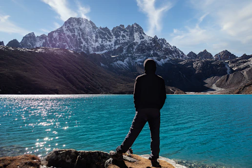 A person in a warm jacket admiring a crystal-clear turquoise lake surrounded by Canadian mountains.