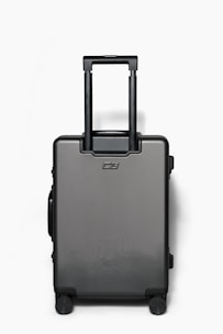 A sleek, modern suitcase standing upright on a city sidewalk with a blurred urban background.