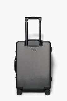 A sleek, modern hard-shell suitcase standing upright on a city sidewalk.