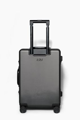 A sleek, modern black suitcase with four wheels and a retractable handle is positioned against a plain white background. The suitcase has a minimalist design with a logo on the front.