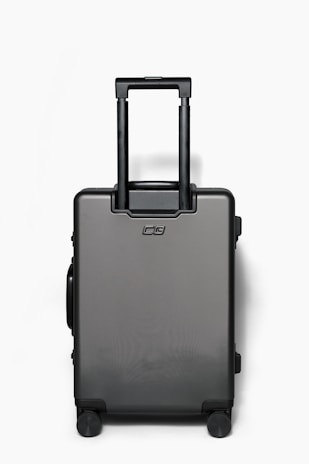 A sleek American Tourister carry-on suitcase standing upright with a modern airport terminal background.