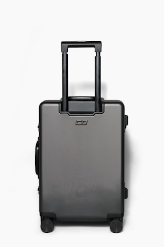 A sleek American Tourister carry-on suitcase standing upright with a modern airport terminal background.