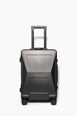 A sleek, sturdy suitcase from phere llc standing upright with a handle extended, set against a soft travel-themed background.
