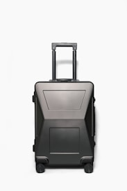 A sleek, modern hardshell suitcase with a dark matte finish, featuring a telescopic handle and four wheels. The suitcase has a minimalistic design with geometric patterns and appears sturdy and durable.