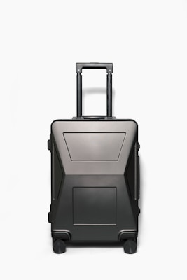 A sleek, modern hardshell suitcase with a dark matte finish, featuring a telescopic handle and four wheels. The suitcase has a minimalistic design with geometric patterns and appears sturdy and durable.