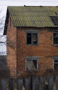 A small brick house with boarded windows and a cracked driveway.