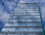 A tall glass building reflecting a partly cloudy sky, with a brand name visible at the top of the structure.