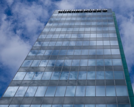 A tall glass building reflecting a partly cloudy sky, with a brand name visible at the top of the structure.