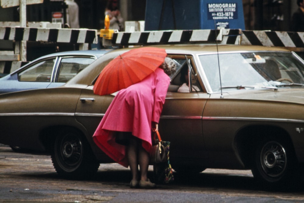 a woman in a pink dress leaning against a car