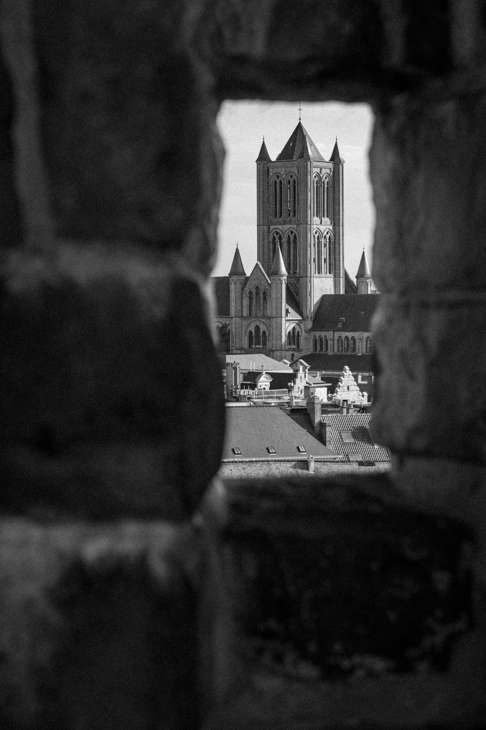 a black and white photo of a cathedral through a hole in a brick wall