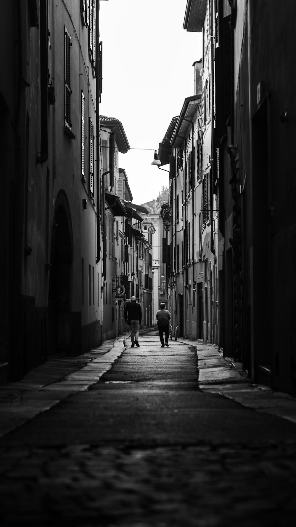 a couple of people walking down a street next to tall buildings