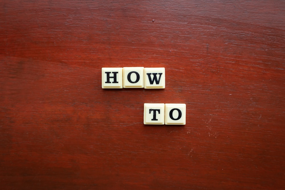 the word how to spelled with scrabble tiles on a wooden surface