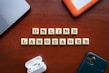 Wooden tiles with letters spelling out 'ONLINE LANGUAGES' are arranged neatly on a wooden surface. Surrounding the tiles, there are a laptop, a hard drive, a smartphone, and wireless earphones.