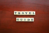 the word travel guide spelled with scrabble tiles