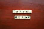 the word travel guide spelled with scrabble tiles
