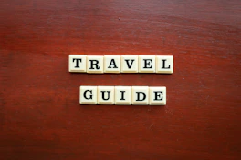 the word travel guide spelled with scrabble tiles