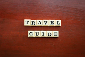 the word travel guide spelled with scrabble tiles